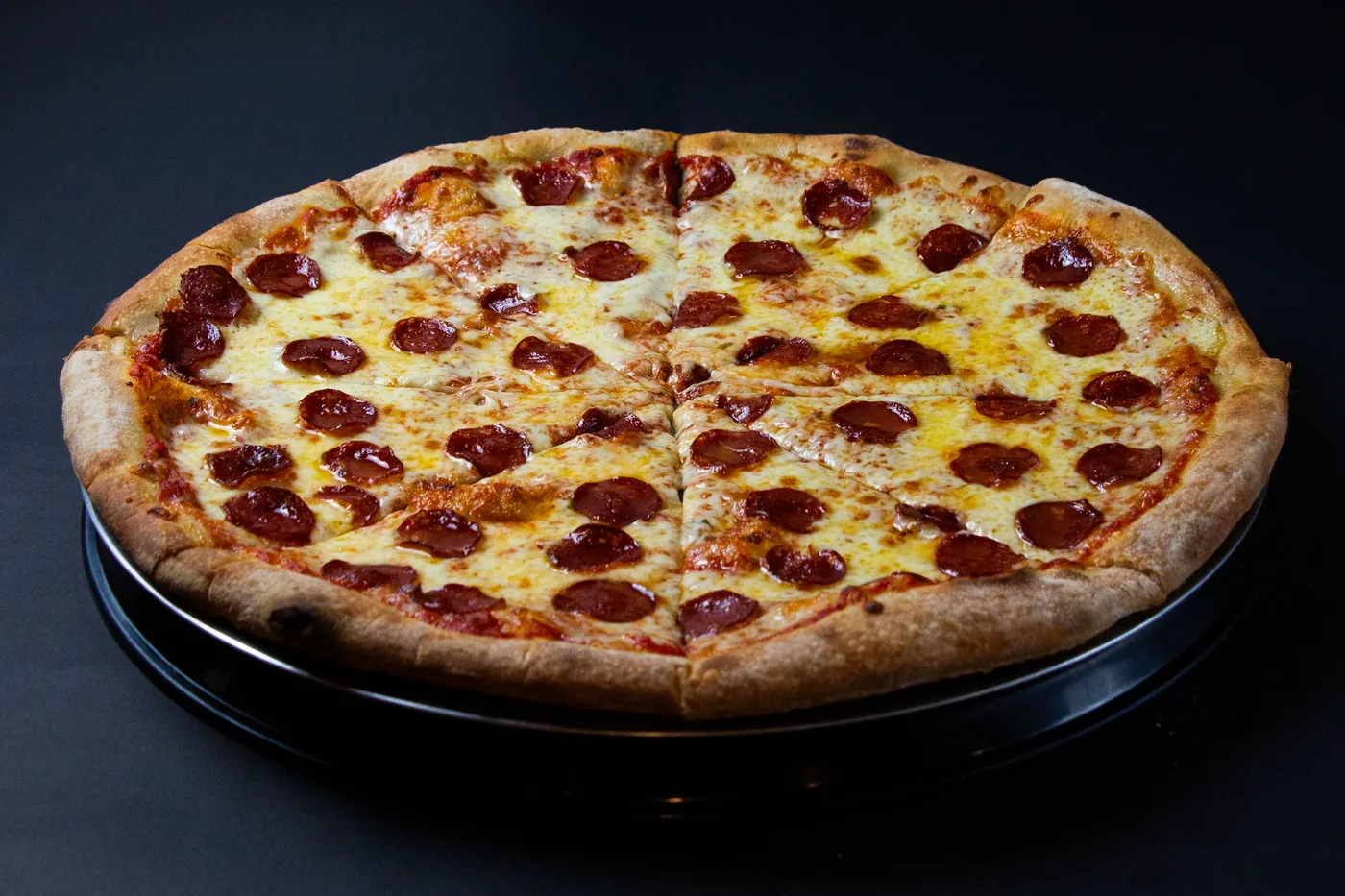 Pizza de pepperoni entera fotografiada en estudio sobre fondo negro