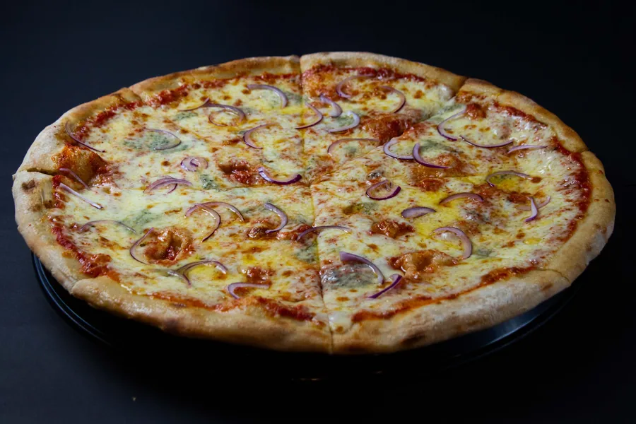 Pizza entera con queso fundido y cebolla morada, fotografiada sobre una bandeja negra