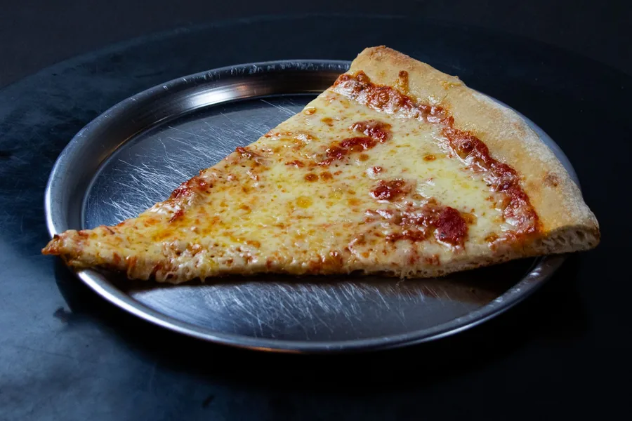 Porción de pizza de muzzarella sobre un plato metálico, fotografiada sobre fondo negro